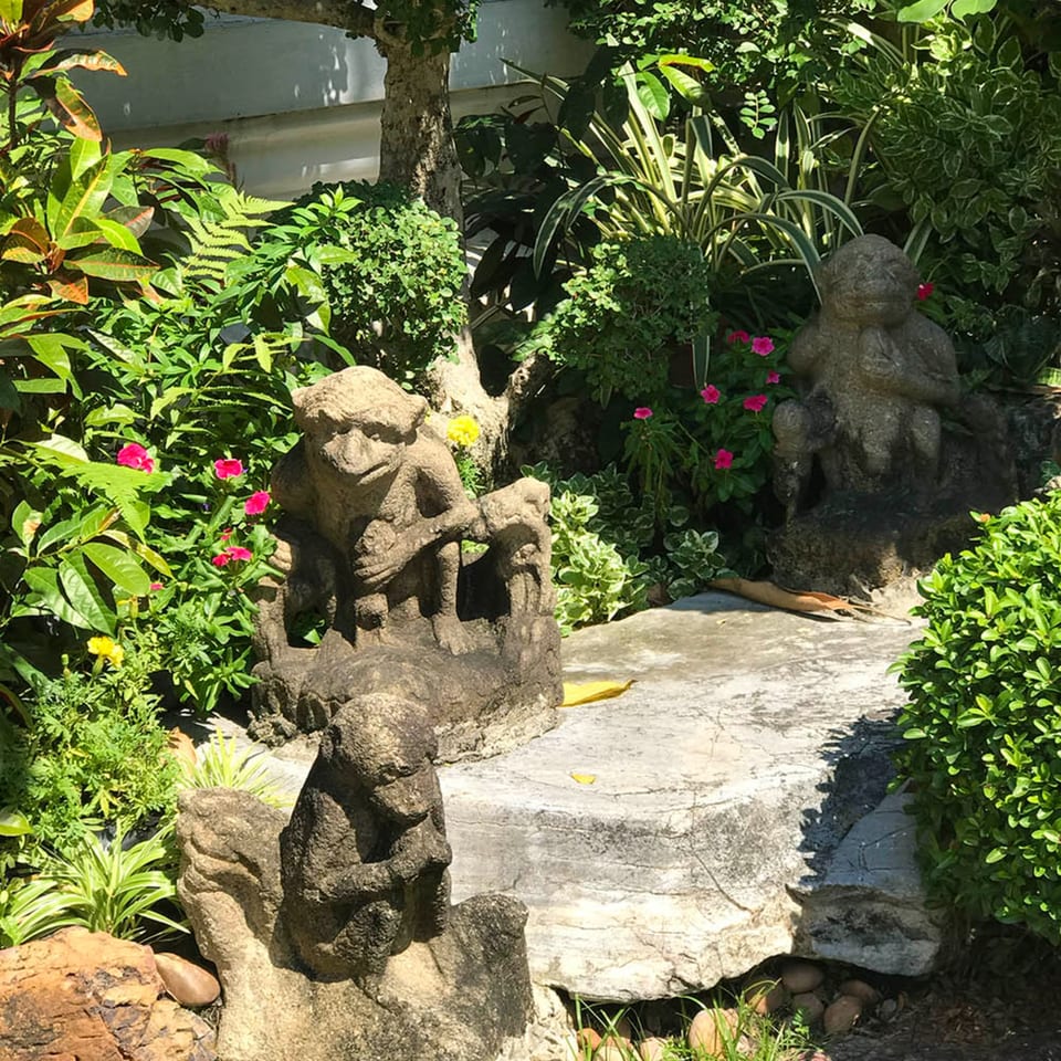 Stone monkey statues nestled among lush green foliage and pink flowers in a garden.