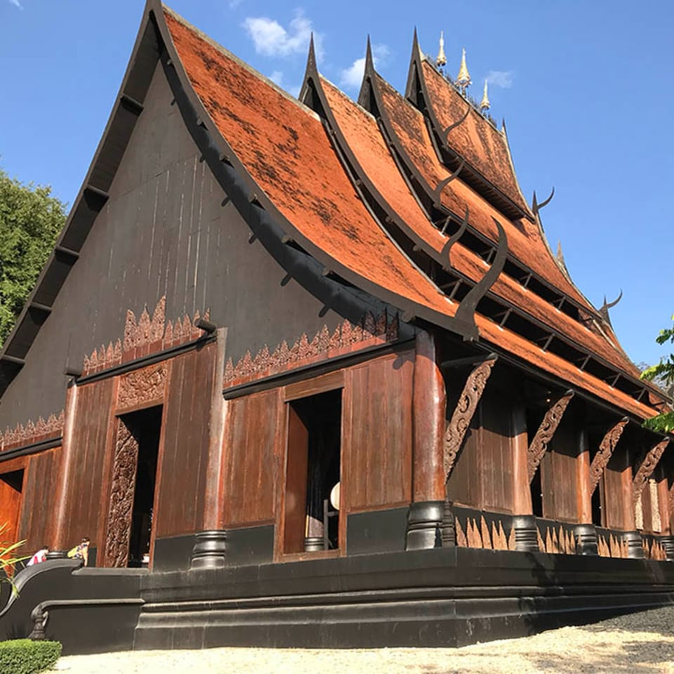 A large, dark wooden building with multiple tiered, red-tiled roofs and ornate carvings under a blue sky.