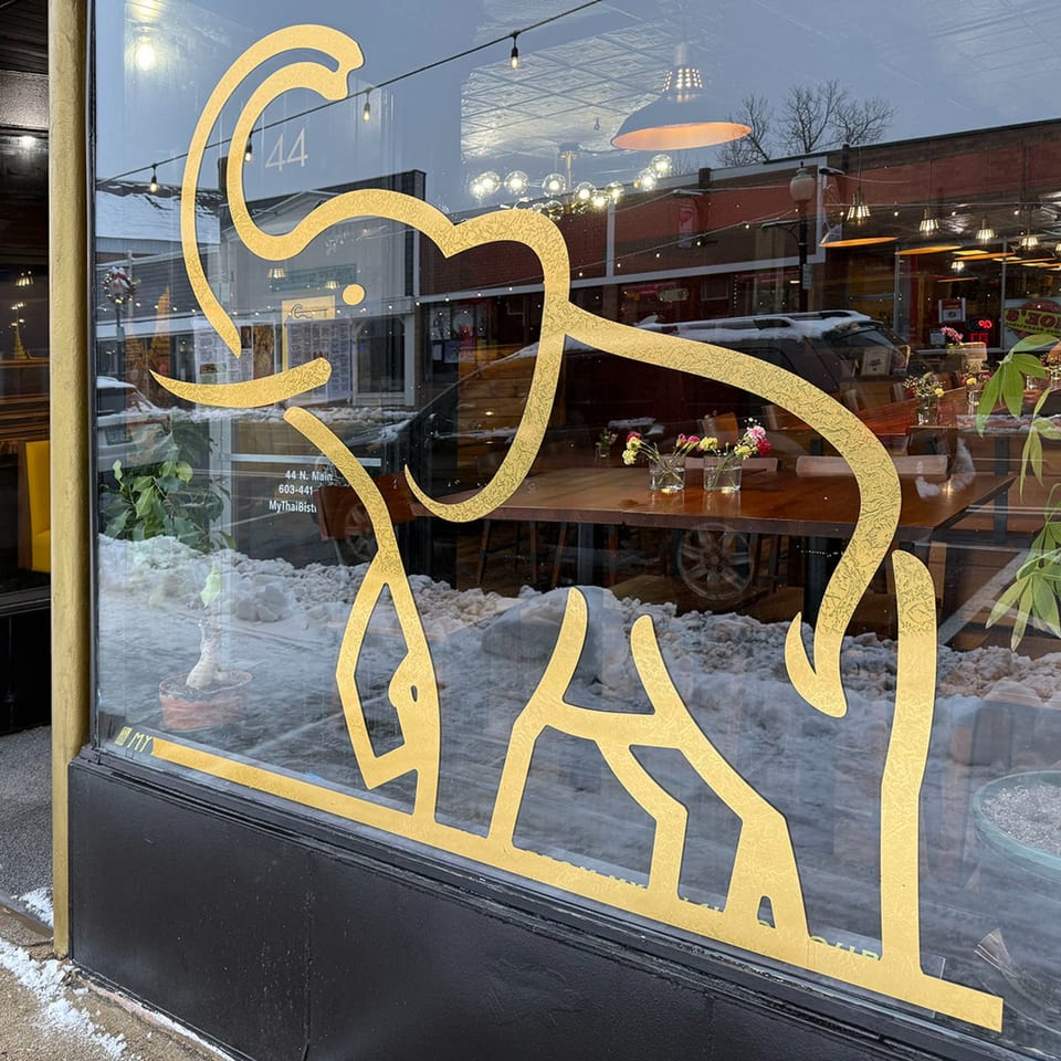 Golden elephant decal on a restaurant window, reflecting a snowy street and interior tables.