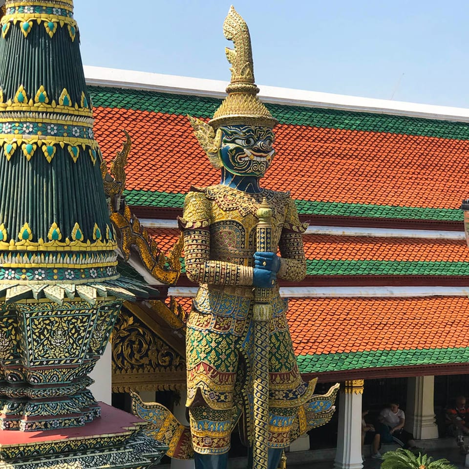 A blue and gold statue of a mythical guardian, with a red and green tiled roof in the background.
