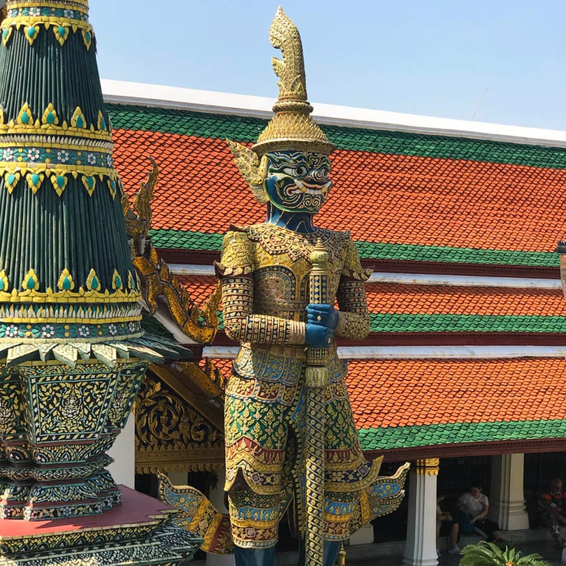 A blue and gold statue of a mythical guardian, with a red and green tiled roof in the background.