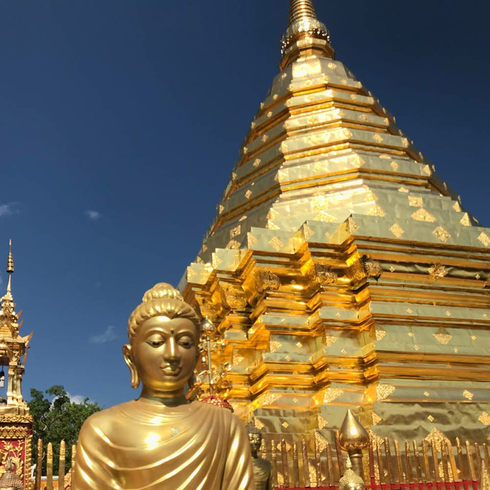 Golden Buddha statue in front of a large, ornate golden pagoda under a clear blue sky.