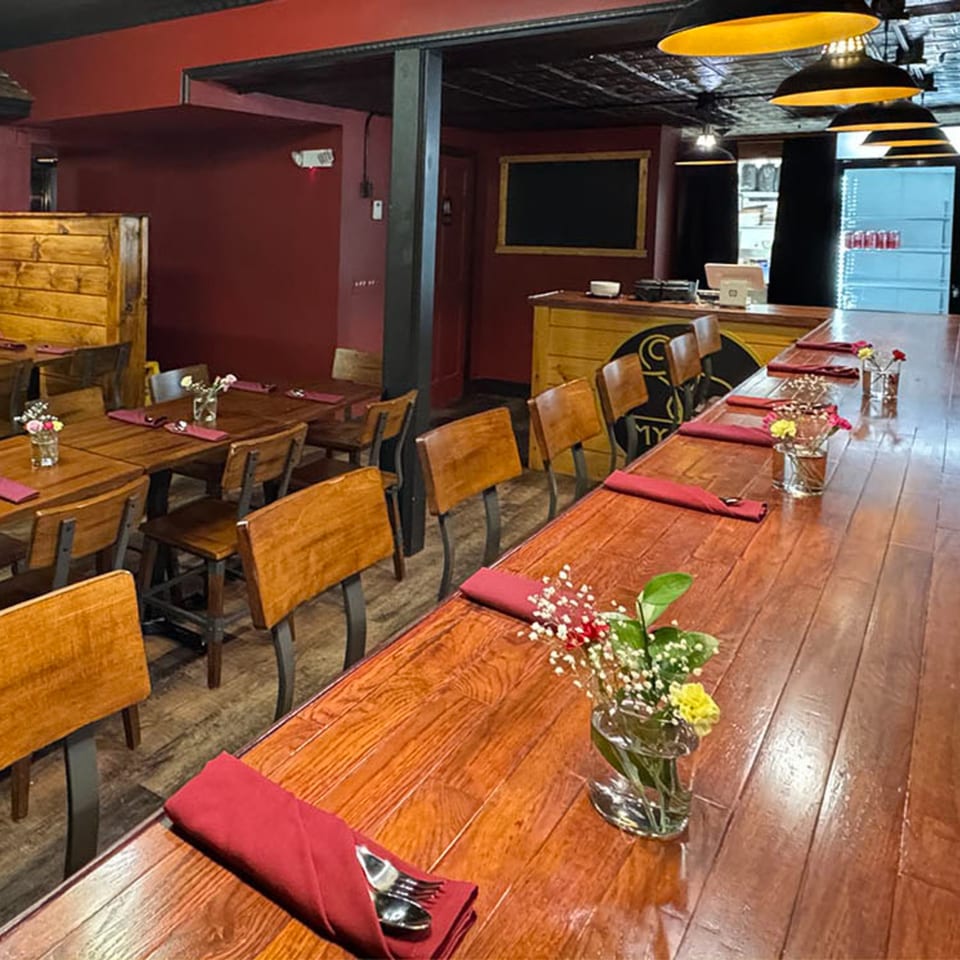 Restaurant interior with wooden tables, red walls, and industrial pendant lights over a long bar.