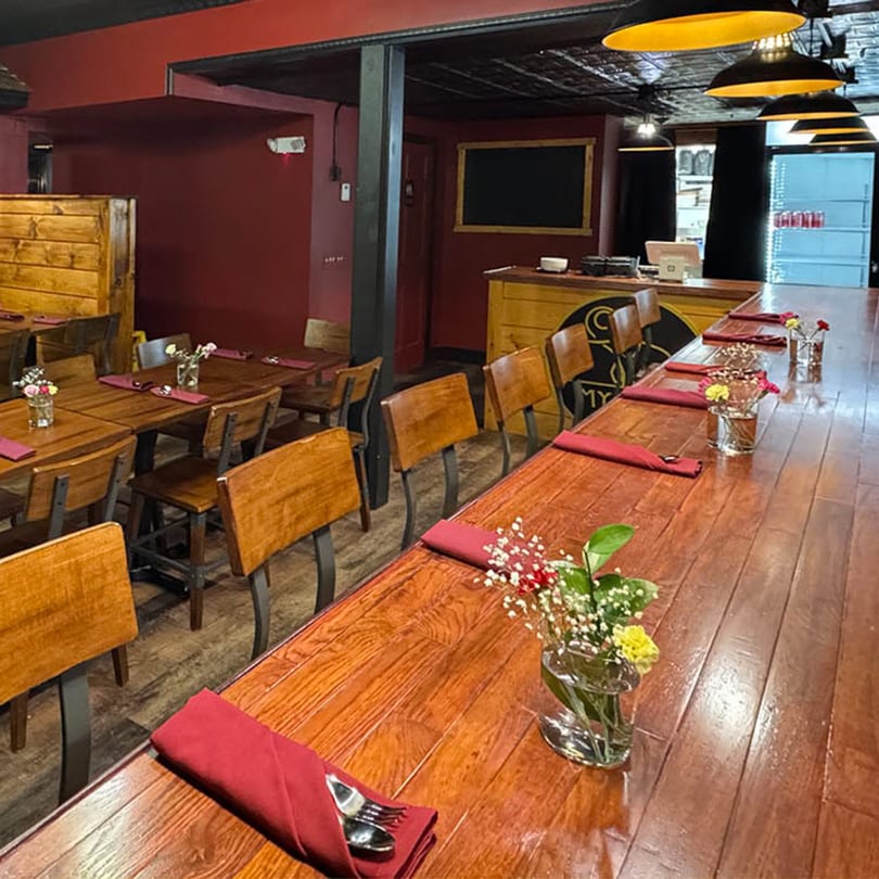 Restaurant interior with wooden tables, red walls, and industrial pendant lights over a long bar.