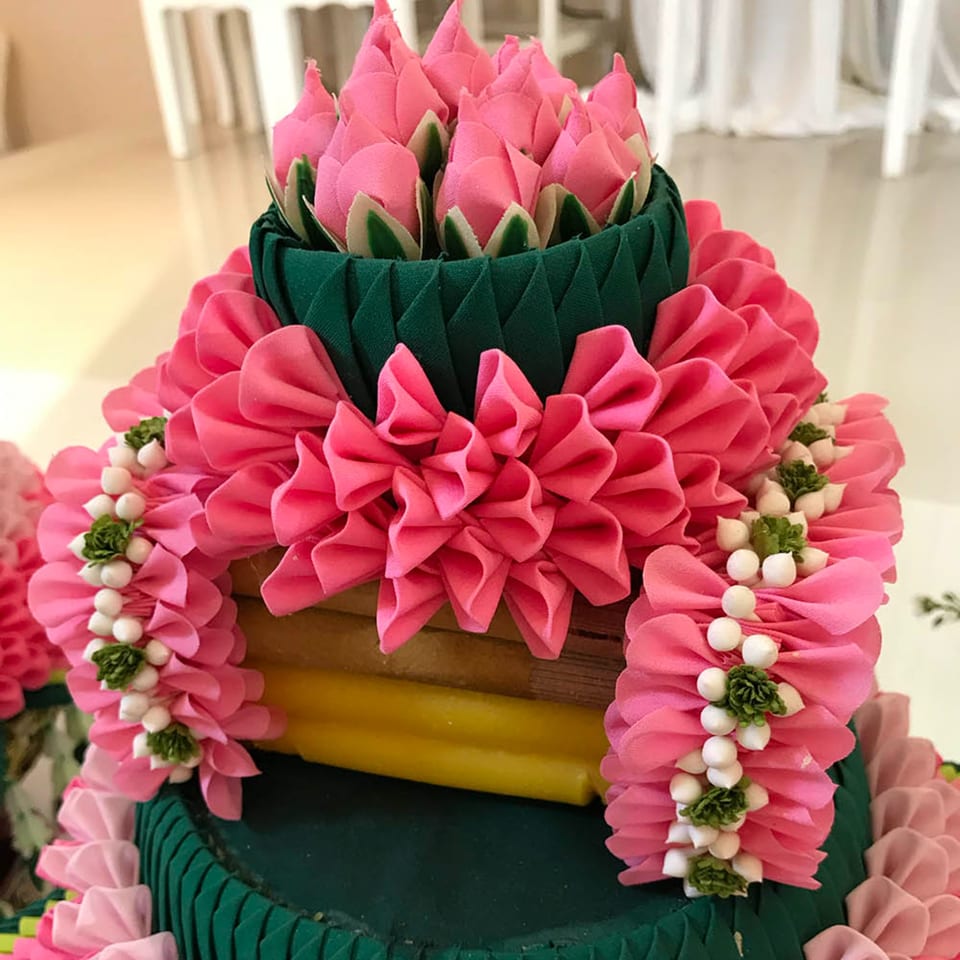 A decorative tiered arrangement with pink fabric lotus buds and garlands, green fabric, and white beads.