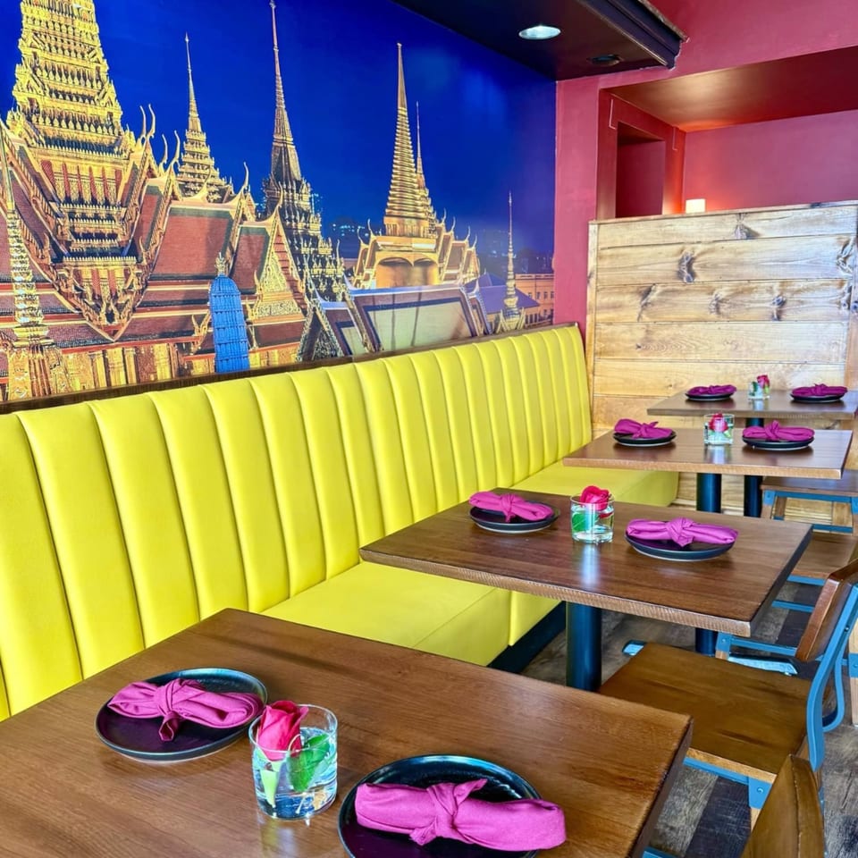 Restaurant interior with yellow booth seating, wooden tables, and a mural of golden temples.