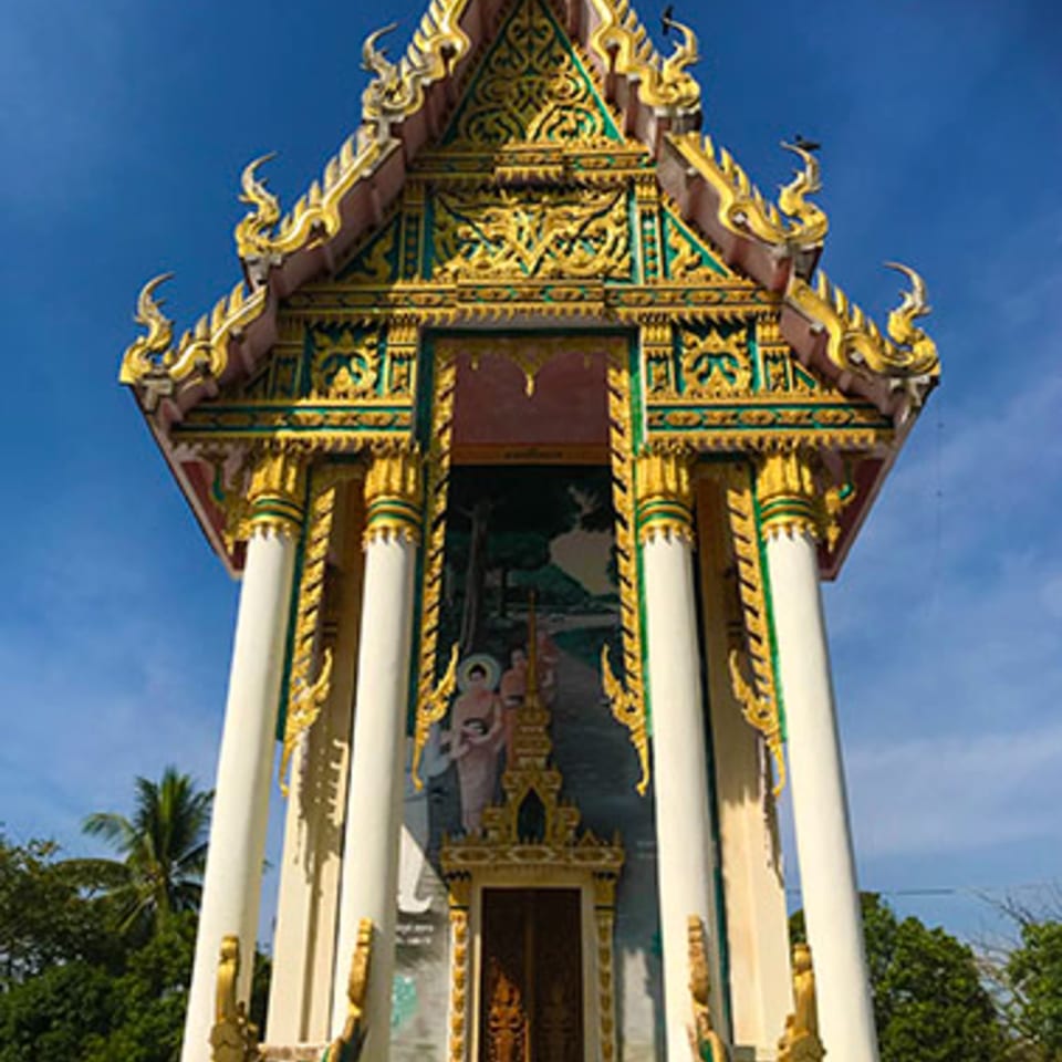 A golden and green ornate temple entrance with white pillars and a mural of figures.