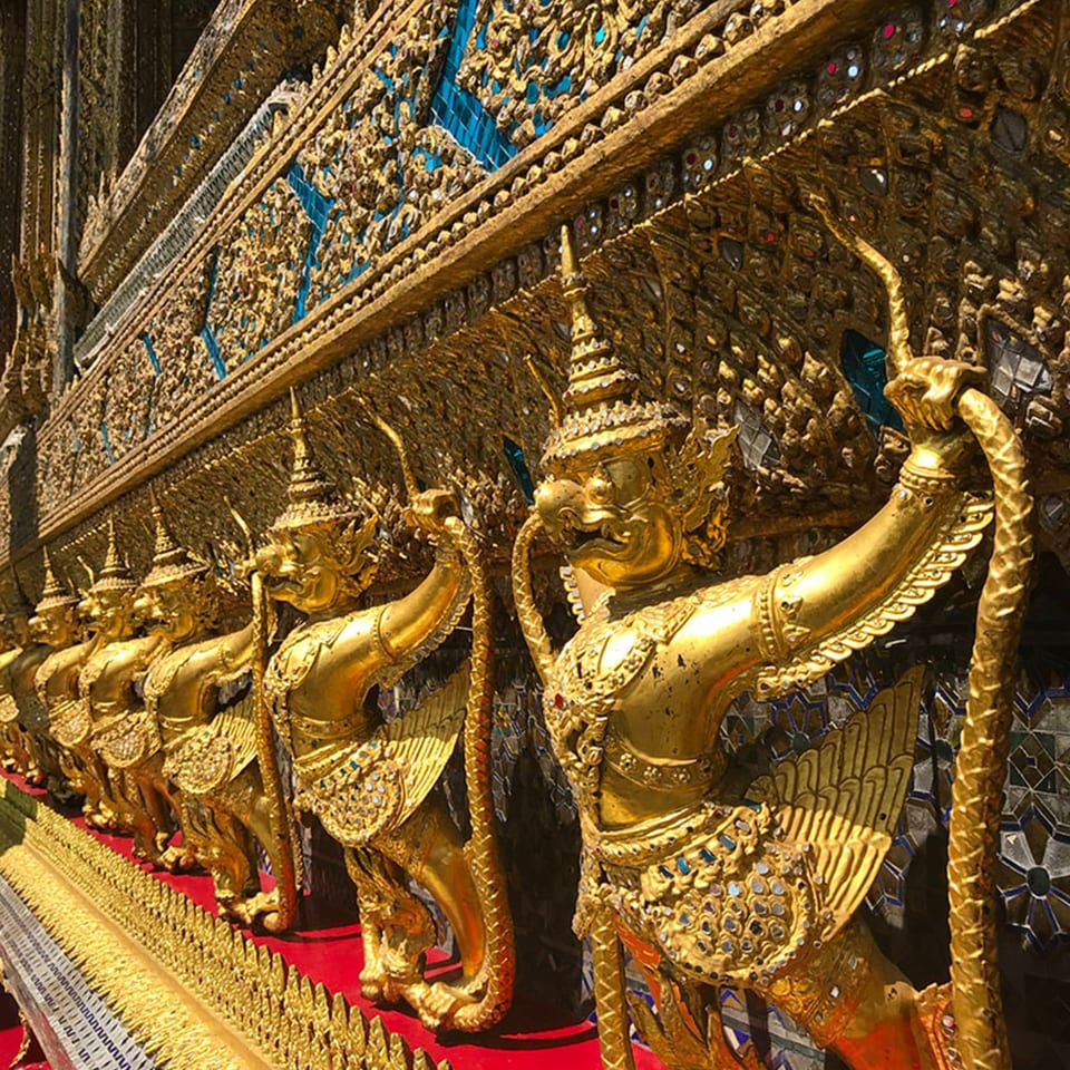 Row of golden Garuda statues with intricate details and blue mosaic accents on a temple wall.