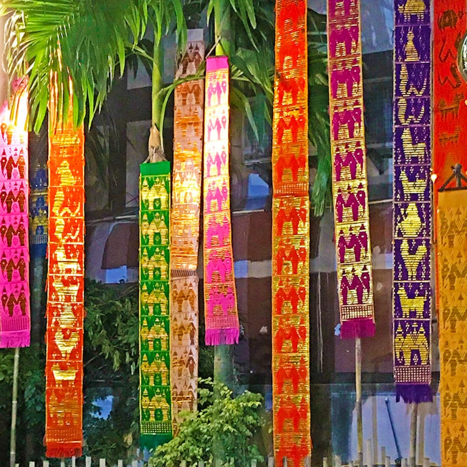 Colorful, patterned banners hang from palm trees, creating a festive outdoor atmosphere.