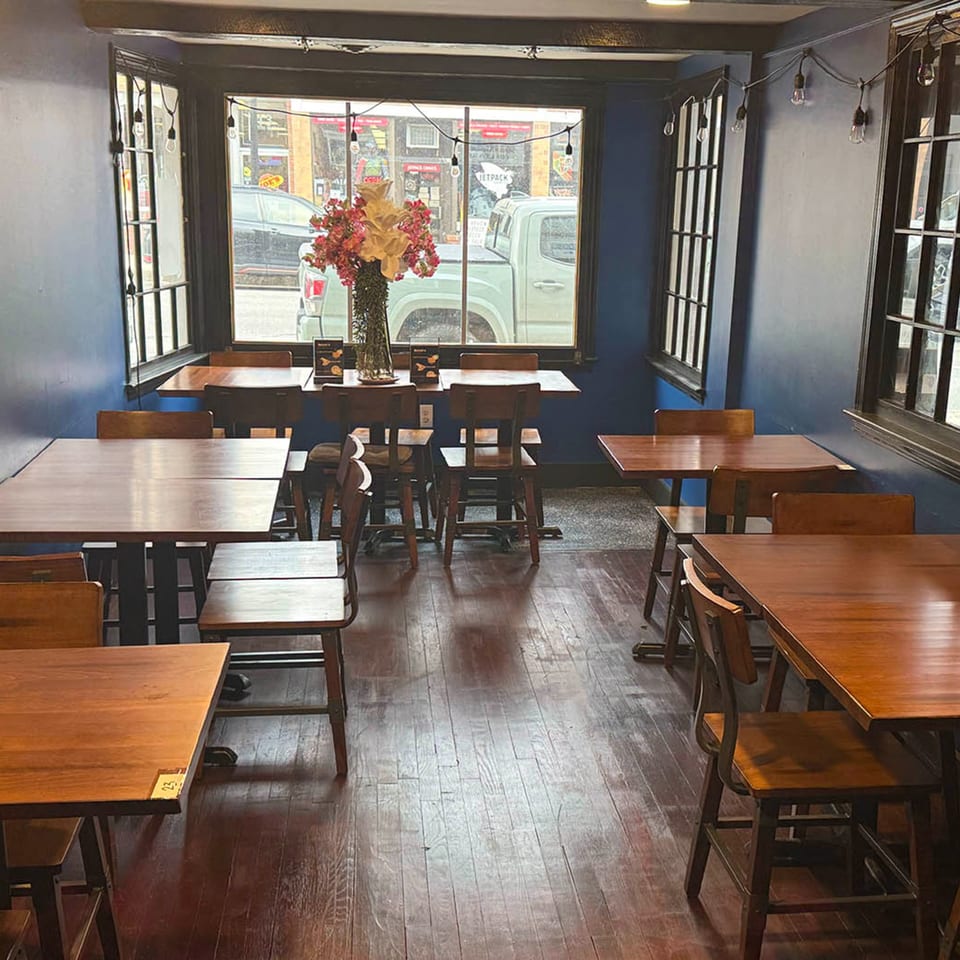 Empty restaurant dining room with wooden tables and chairs, blue walls, and large windows.
