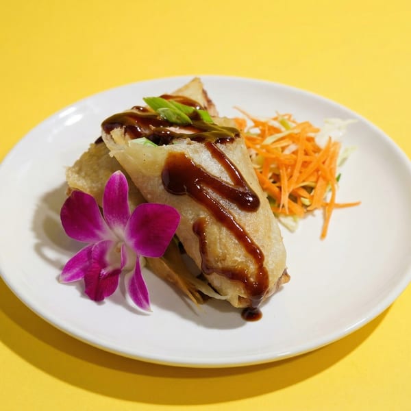 Crispy spring rolls drizzled with dark sauce, garnished with green onions, shredded carrots, and a purple orchid.
