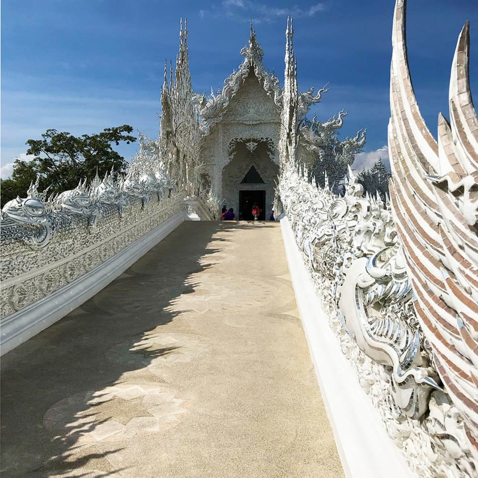 A white ornate temple with a long walkway leading to its entrance under a blue sky.