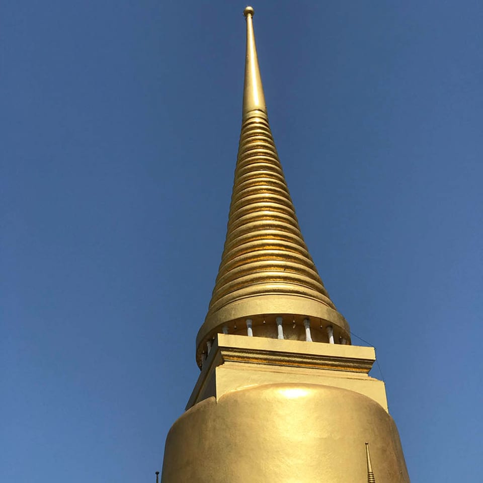 Golden spire of a Buddhist temple against a clear blue sky, viewed from below.