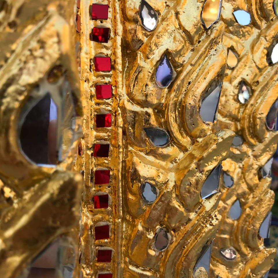 Intricate golden carving with red and mirrored accents, reflecting light and surrounding details.