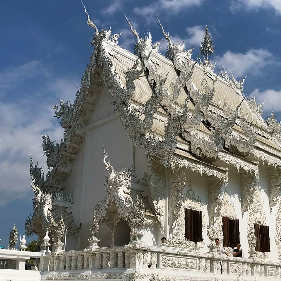 Intricate white temple with ornate roof details and dark windows under a blue sky.